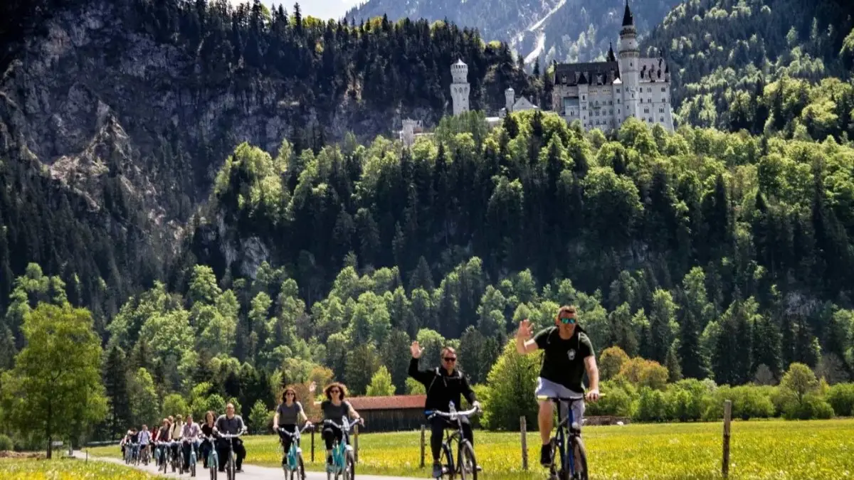 Tourists riding the bikes near Neuschwanstein Castle with the Alpine views Tourists riding the bikes near Neuschwanstein Castle with the Alpine views