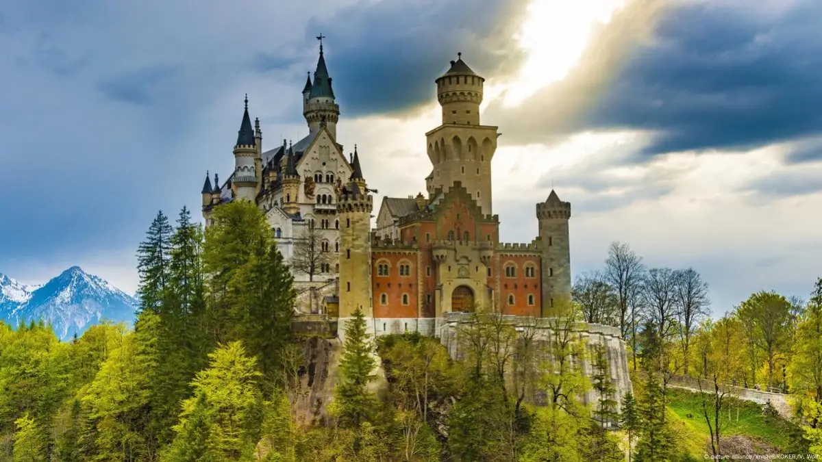Neuschwanstein Castle on a bright day with Alpine mountains as the backdrop